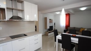 Una cocina moderna con armarios blancos, un comedor con mesa blanca y sillas negras, y una sala de estar con sofá y cortinas rojas.