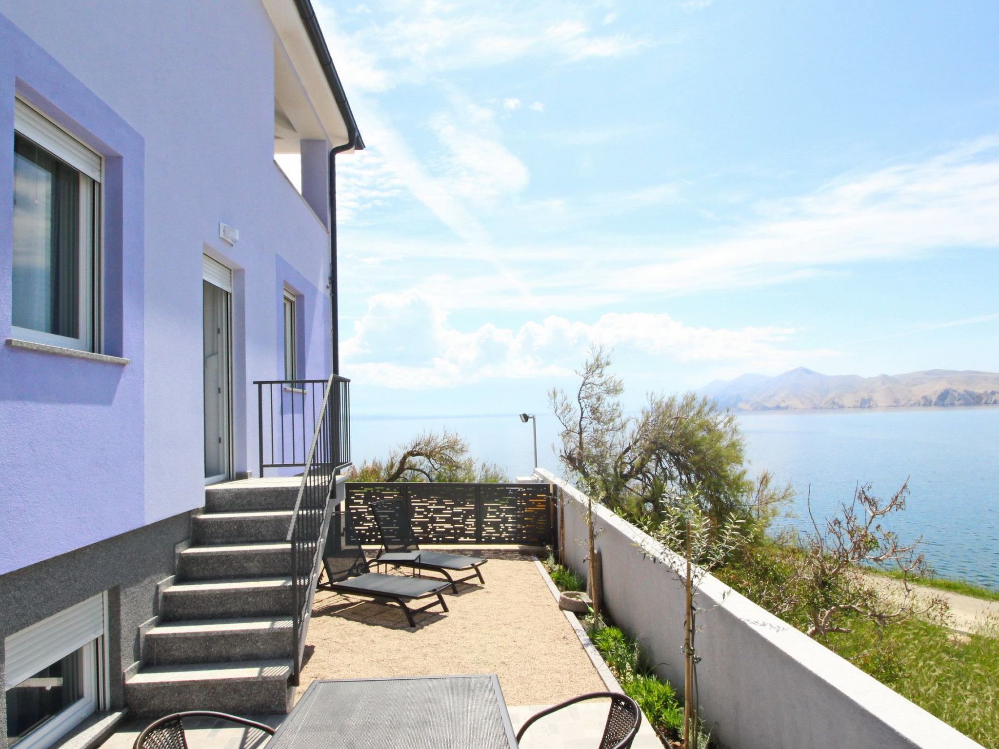 A building with a balcony overlooking a lake, featuring outdoor seating and a staircase.