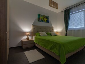 Ein Schlafzimmer mit einem Bett, Nachttischen, einem Gemälde und einem Fenster mit Vorhängen.
