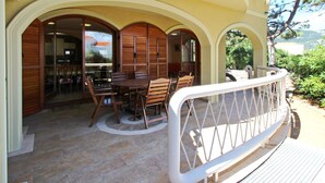Un espace extérieur abrité, aménagé pour les repas, avec une table et des chaises, une rambarde blanche et une vue sur le paysage environnant.