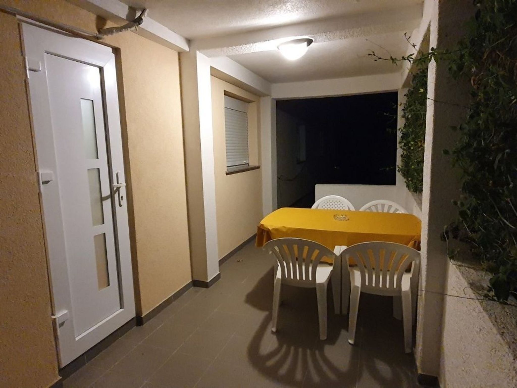 Eine kleine Terrasse im Freien mit Tisch und Stühlen, einer weißen Tür und einem Fenster mit Jalousien.
