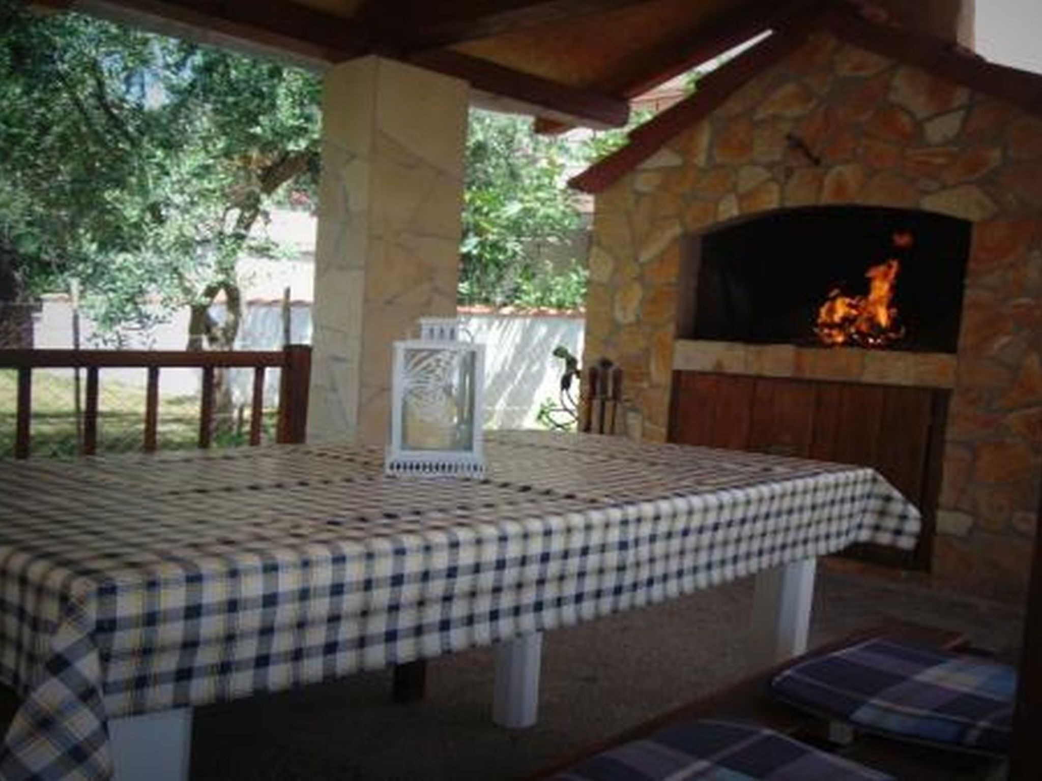Eine Terrasse im Freien mit Kamin aus Stein, kariertem Tischläufer und Bänken.
