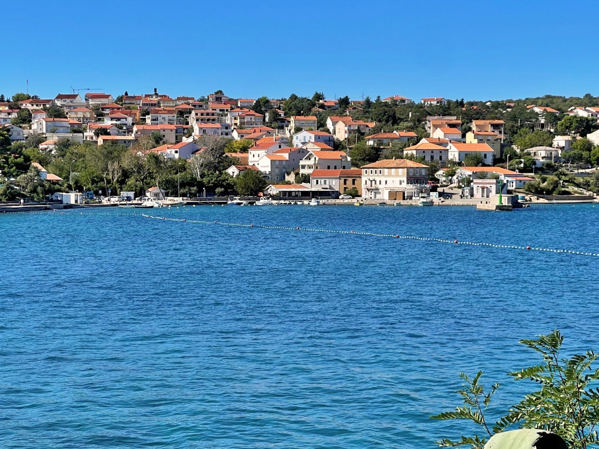 Uma cidade costeira com edifícios à beira-mar, um mar azul límpido e uma área de cais visível.