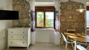Une pièce avec un mur en pierre, une table à manger en bois avec des chaises, un meuble blanc avec des tiroirs et un téléviseur fixé au mur.
