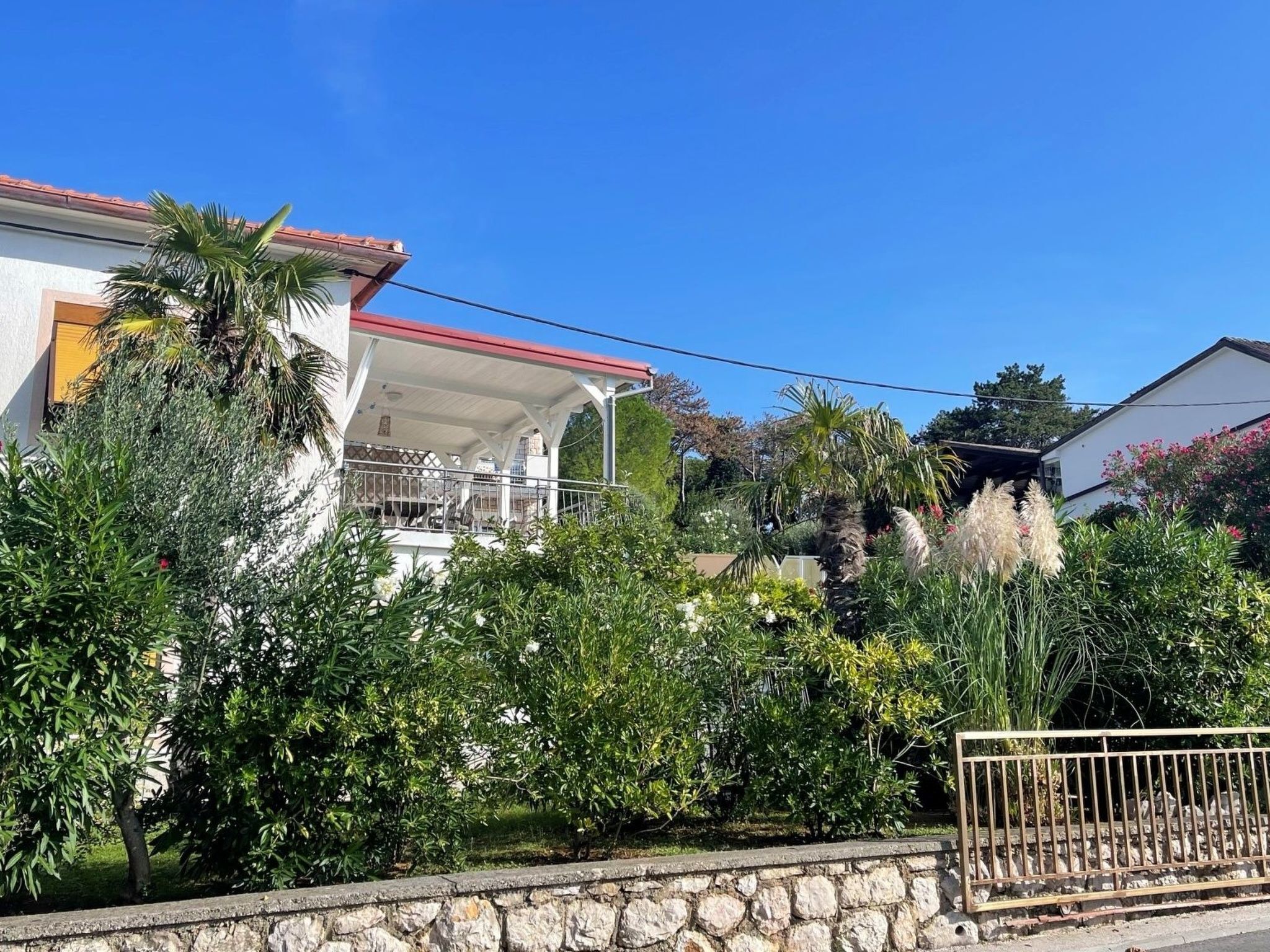 A house with a covered porch, surrounded by lush greenery and a stone wall.