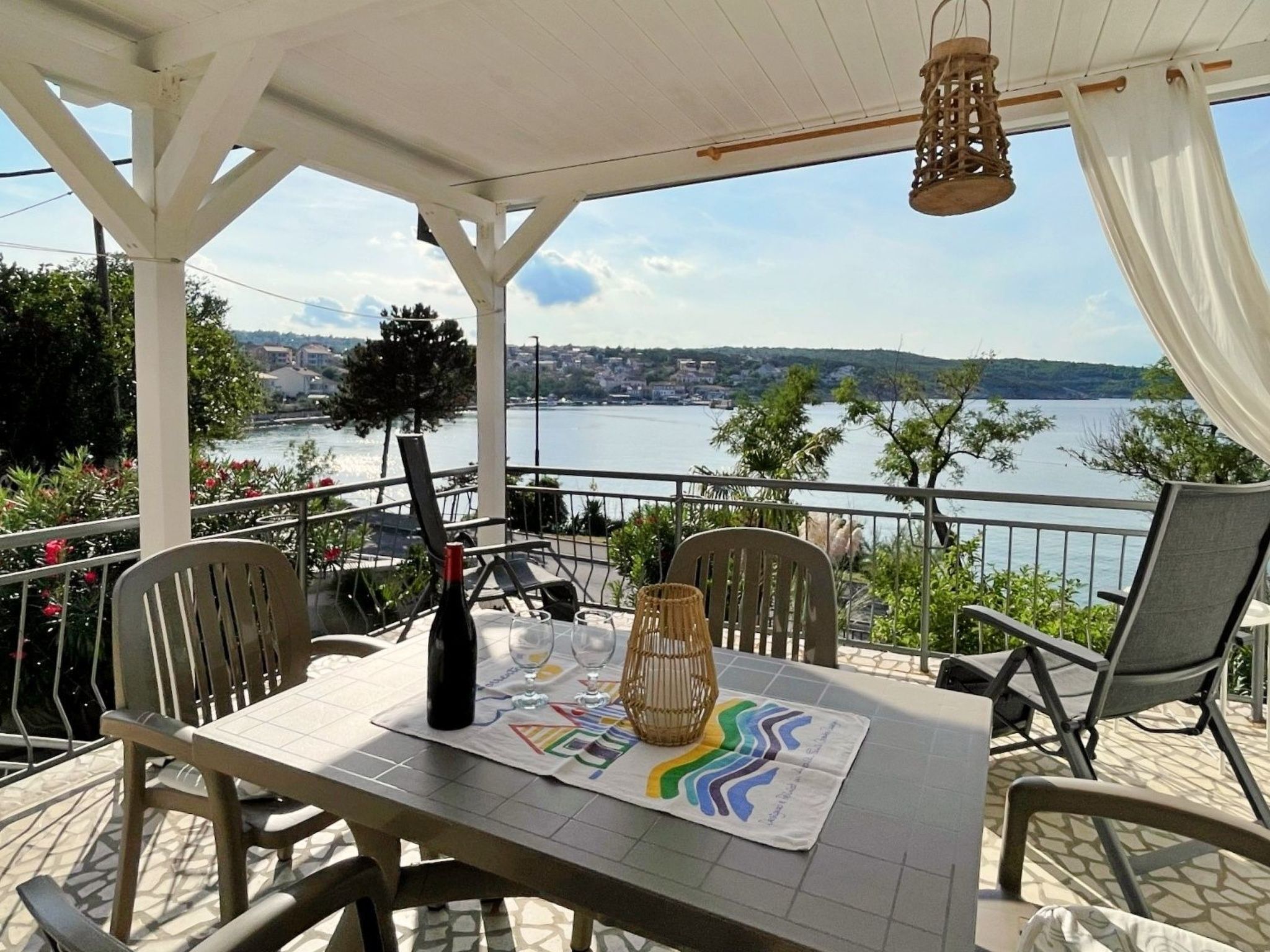 En terrass med ett bord dukat för två personer, med utsikt över en sjö eller ett annat vattendrag och en avlägsen stadsbild.