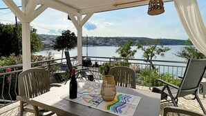 Une terrasse avec une table dressée pour deux personnes, offrant une vue sur une étendue d’eau et sur le lointain paysage urbain.