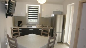Eine kleine Küche mit Esstisch, Stühlen, einem Kühlschrank und einem Fenster mit Jalousien.