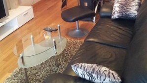 Ein Wohnzimmer mit einer schwarzen Ledersofa, einem Glastisch und einem Essbereich mit Holztisch und Stühlen.