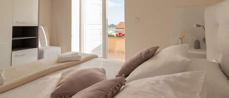 Quarto com cama, almofadas, mesa de cabeceira, guarda-roupa e porta de vidro corrediça para uma varanda externa.