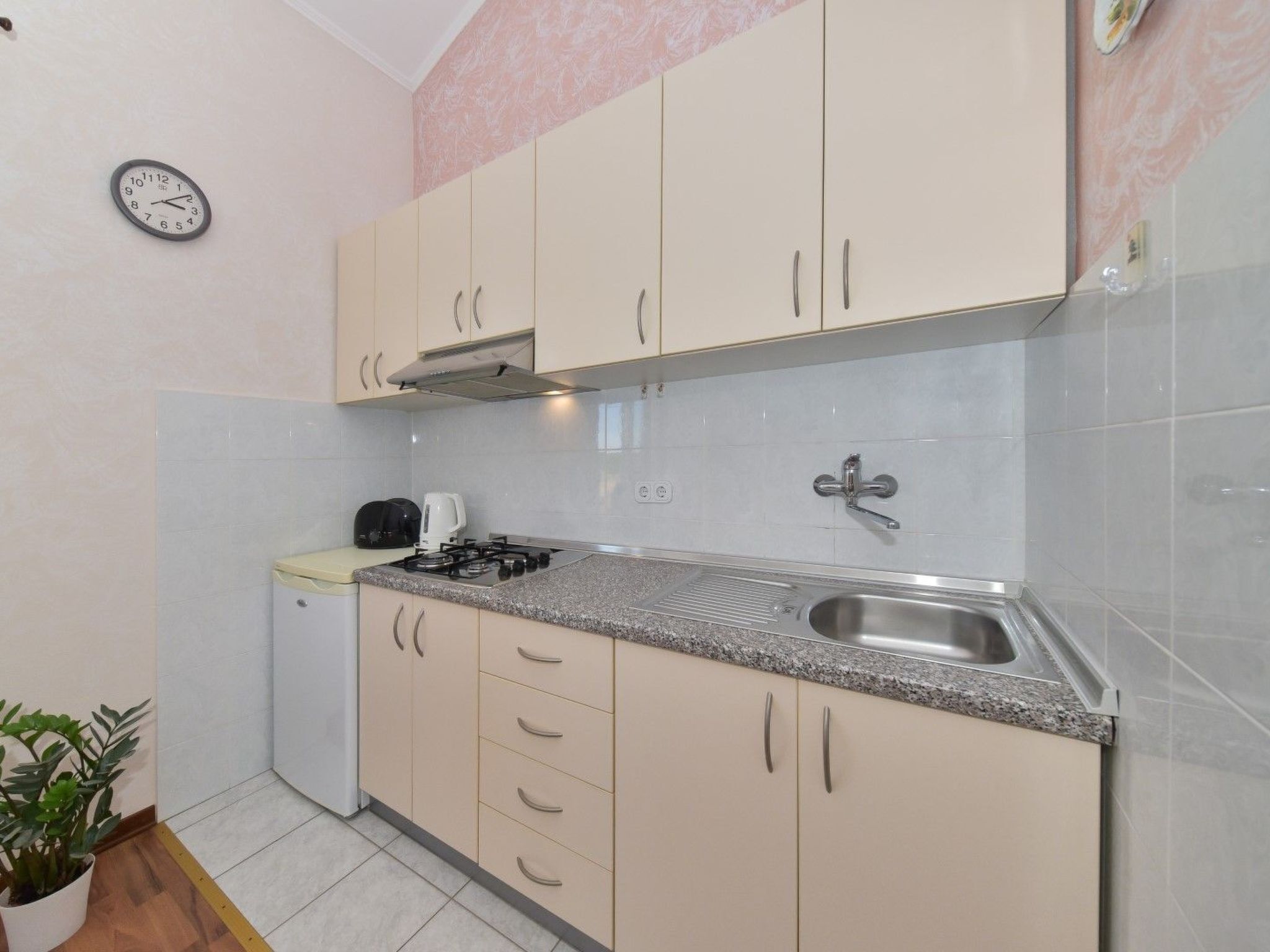 A compact kitchen with beige cabinets, a stainless steel sink, a gas stove, and a small refrigerator.