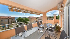 A balcony with a glass table, chairs, and a view of the sea and buildings. - Apartment  Medanic 3 by Interhome (Privlaka)