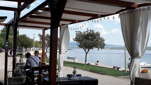 Un espace extérieur aménagé avec des tables et des chaises, offrant une vue sur une étendue d’eau et un arbre.