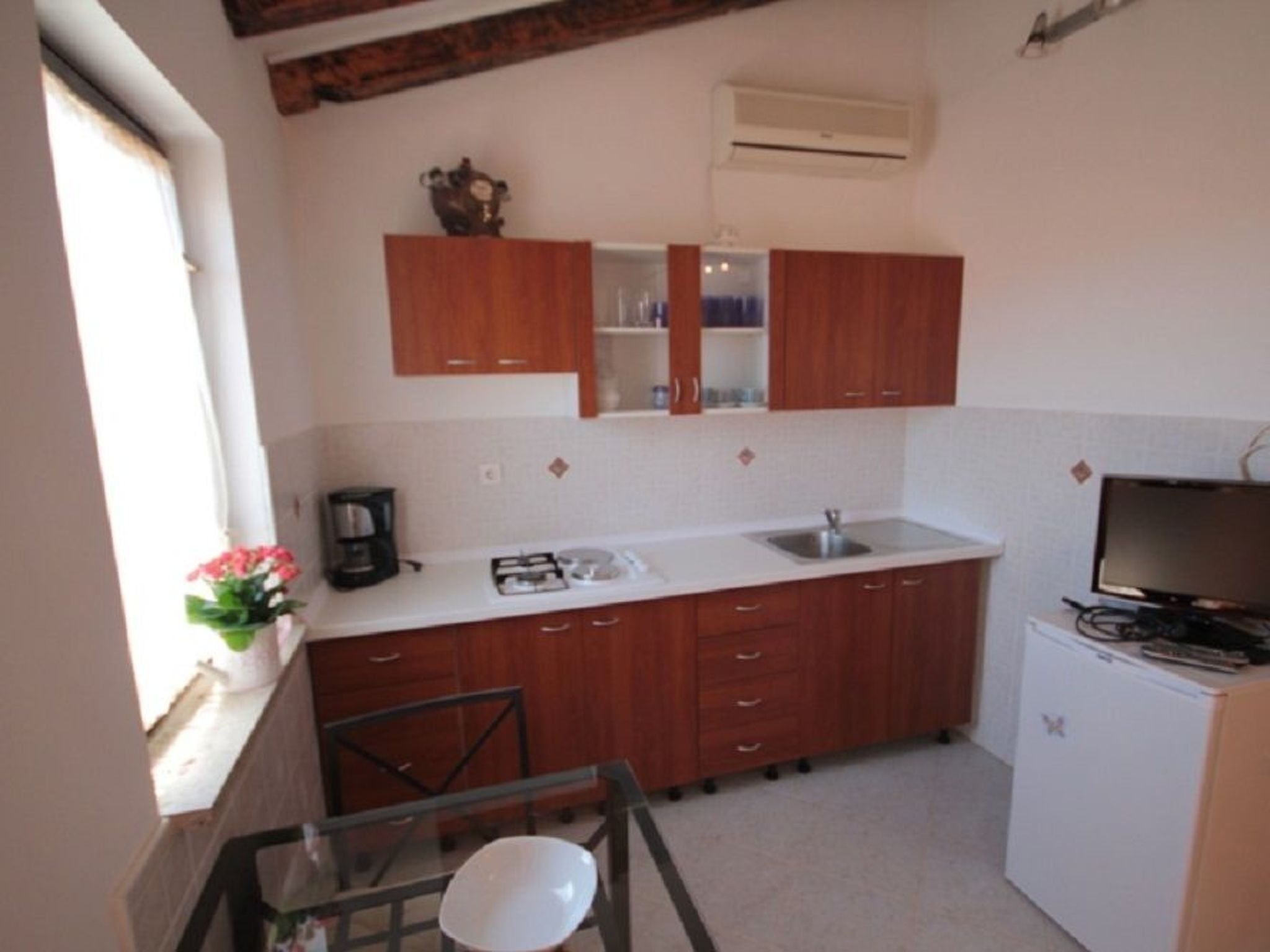 A compact kitchen with wooden cabinets, a white countertop, a sink, a coffee maker, and a television.
