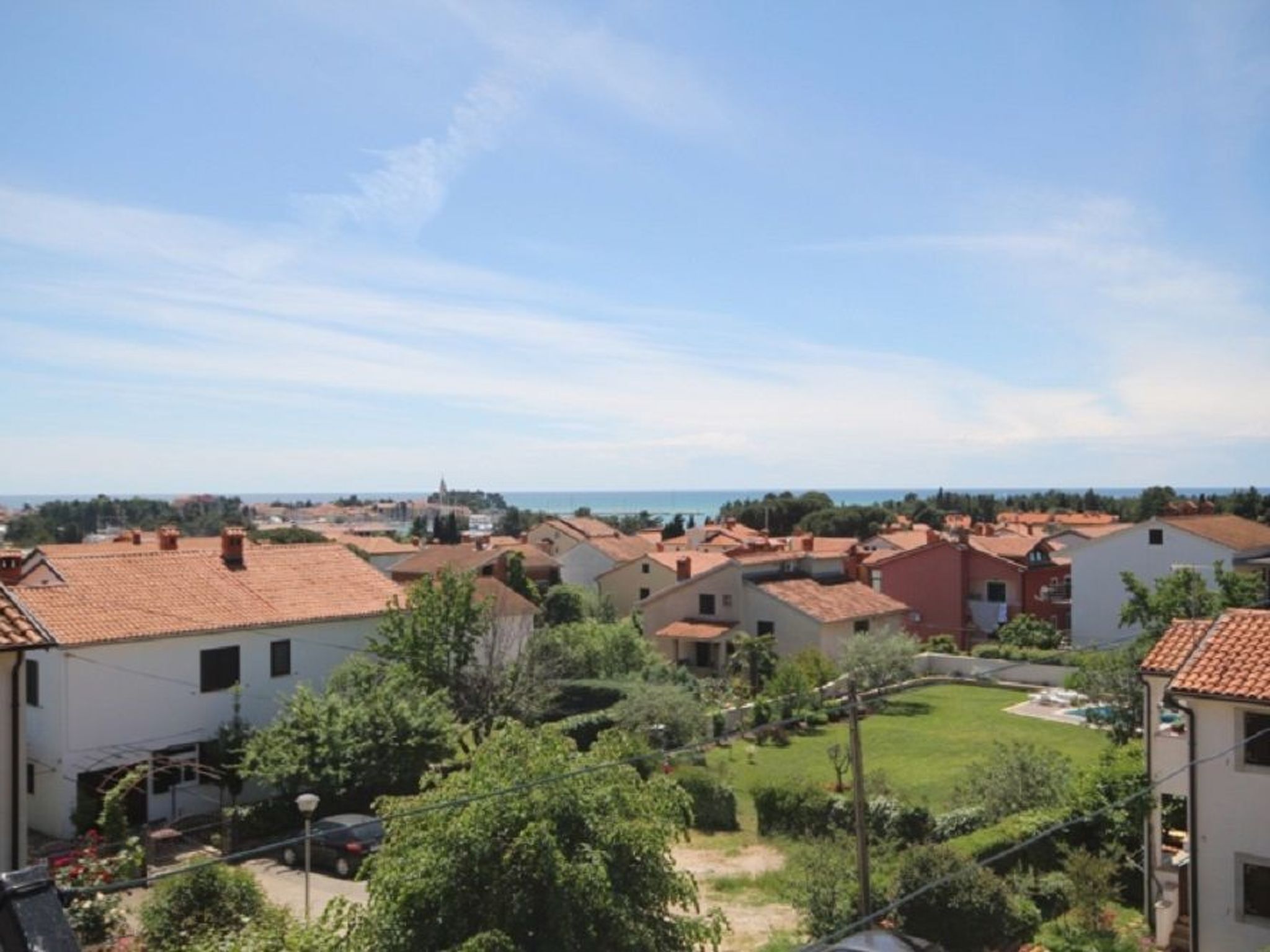 A residential area with terracotta-roofed houses, a grassy yard, and a distant view of the sea.