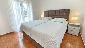 Hotellihuone, jossa on suuri sänky, kaksi yöpöytää valaisimineen ja ikkunasta avautuva näkymä vehreään maisemaan.
