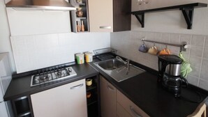 A compact kitchen with a gas stove, a sink, and a coffee maker. There are cabinets and a shelf with kitchenware. - Wohnung in Novigrad by Interhome (Novigrad (Istra))