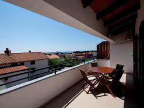Een balkon met een tafel en stoelen, met uitzicht op een woongebied met rode dakpannen.