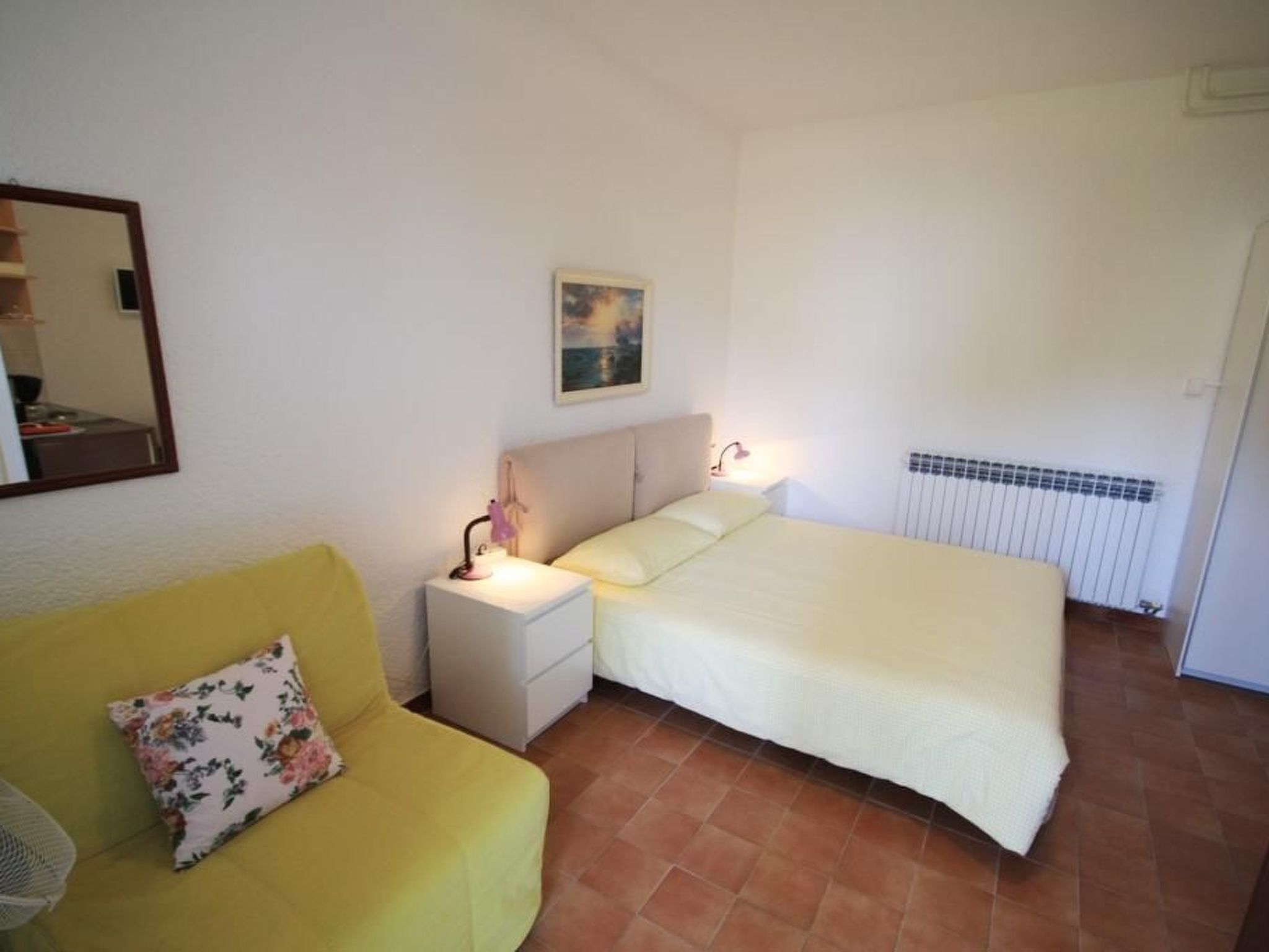 Un dormitorio con cama, mesita de noche, lámpara de noche, sillón y radiador.