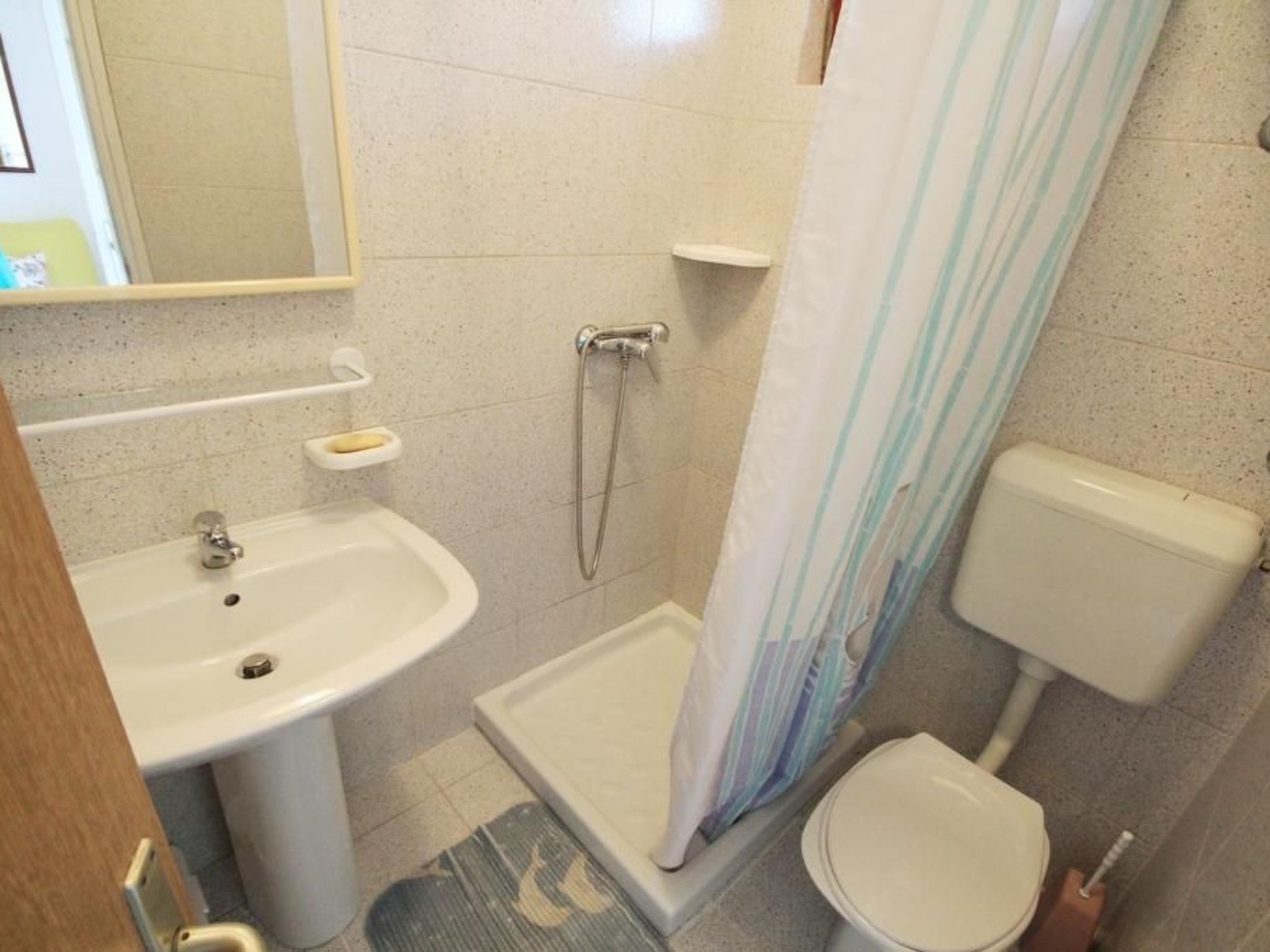 Un bany petit amb un lavabo, vàter, dutxa i mirall.