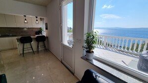 Een moderne keuken met een groot raam, een zithoek met twee zwarte stoelen en uitzicht op zee.