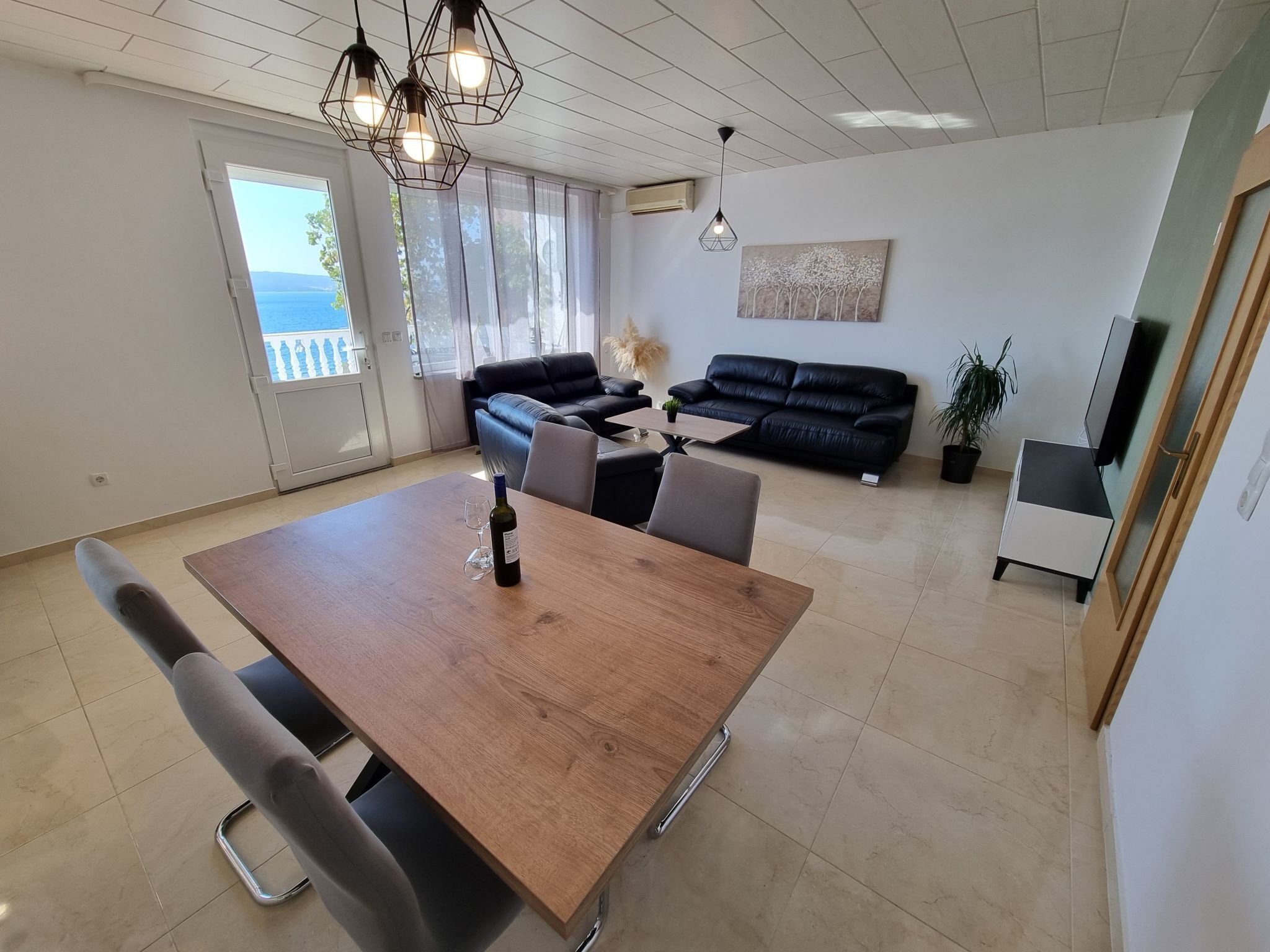 Uma sala de estar moderna com área de jantar, com mesa de madeira, sofás de couro preto e uma janela grande com vista.