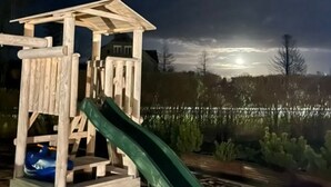 A wooden play structure with a slide, set against a backdrop of a dark sky and a body of water. - Komfortable Wohnung mit Garten, in der Nähe des Meeres by Interhome (Sarbinowo)