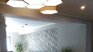 Un vaste espace de vie doté d’un parquet en bois disposé en motif chevrons, d’un canapé d’angle gris et d’un mur décoratif orné de motifs hexagonaux.
