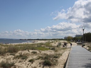 Hiekkainen ranta, jossa on kävelyreitti, ruohokasvustoisia dyynimäkiä ja vesialue.