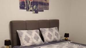 Un dormitorio con una cama grande, dos mesitas de noche con lámparas, suelo de madera y un cuadro floral en la pared.