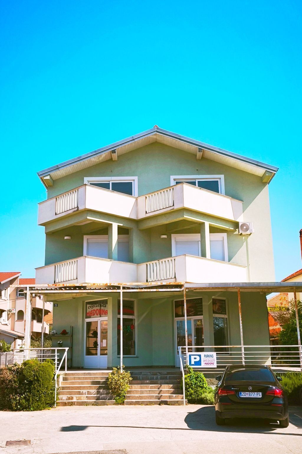 A two-story building with a balcony on the upper floor, a covered entrance, and a parking sign.