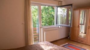 Un dormitorio con una cama grande, un ventanal con vistas a la vegetación, un radiador y un armario.