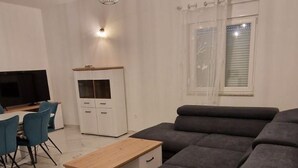 Un saló modern amb un sofà seccional gris, una taula de centre de fusta, un televisor i una zona de menjador amb cadires.