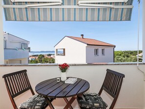 A balcony with a table and chairs, a striped awning, and a view of a white house with a red roof. - Apartment Bluebell Zadar mit privatem Parkplatz by Interhome (Zadar)