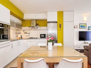 A modern kitchen with white cabinets, a glass-top dining table, and a yellow accent wall. - Apartment Bluebell Zadar mit privatem Parkplatz by Interhome (Zadar)