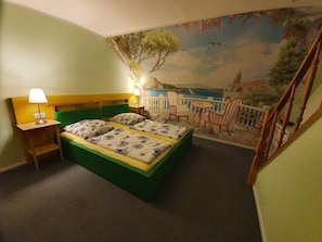 Ein Schlafzimmer mit einem Bett, zwei Nachttischen, einer Lampe und einem Wandbild mit einer Strandansicht.