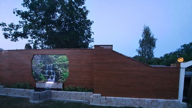 Ein modernes Gebäude mit Holzfassade, einem angelegten Garten und einem Wasserfall.