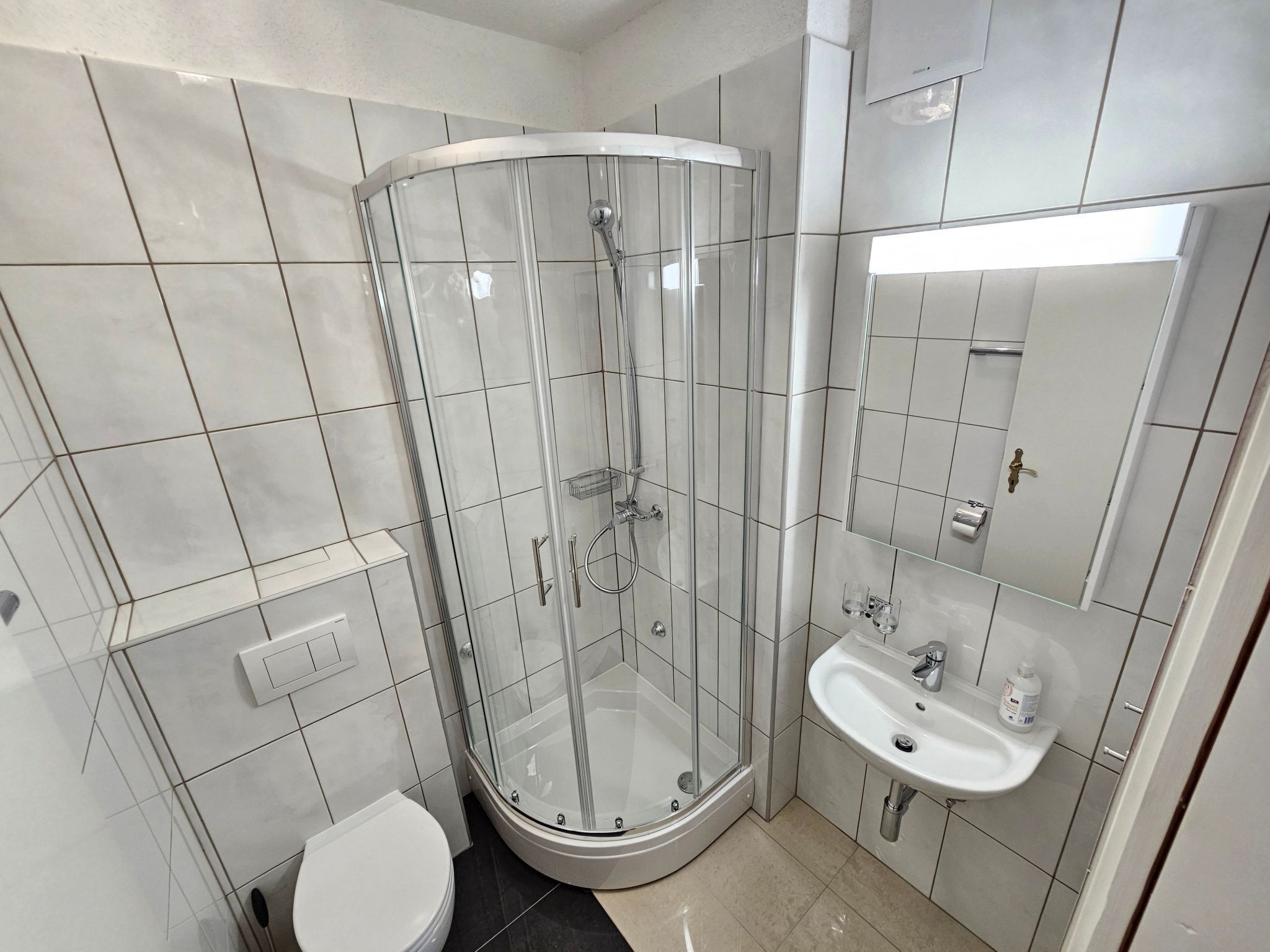 Et moderne badeværelse med et glasafskærmet brusebad, et hvidt toilet og en vask med et spejl over.