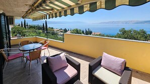A balcony with wicker furniture, a table, and chairs, overlooking a scenic view of a body of water and distant mountains. - Wohnung mit Meerblick, 150 m vom Strand entfernt by Interhome (Novi Vinodolski)
