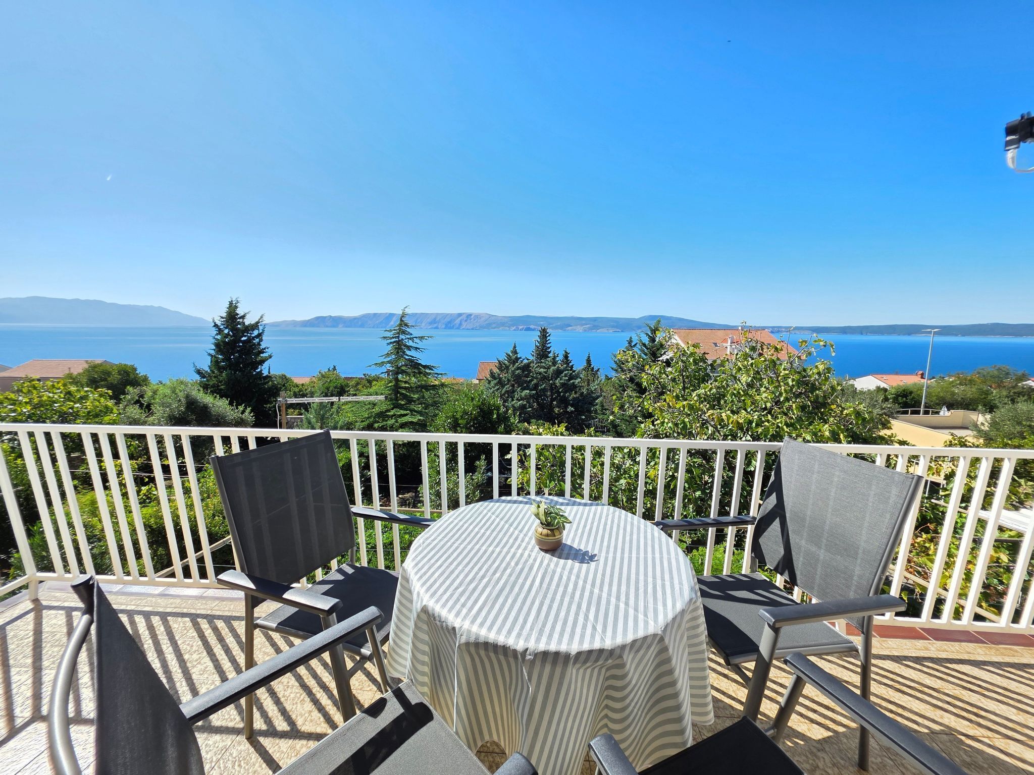 A terrace with a table and chairs, overlooking a scenic view of the sea and mountains.