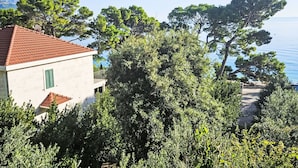 A building with a red-tiled roof, surrounded by dense greenery and overlooking a body of water. - Wohnung "Apartman für 4 Personen" by Interhome (Brela)