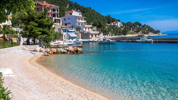 A coastal beach with clear turquoise waters, a sandy shore, and buildings with balconies overlooking the sea. - Wohnung "Apartman für 4 Personen" by Interhome (Brela)