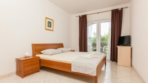 A bedroom with a bed, a nightstand, a television on a stand, and a balcony with curtains. - Apartment Luna by Interhome (Trogir/Okrug Donji)