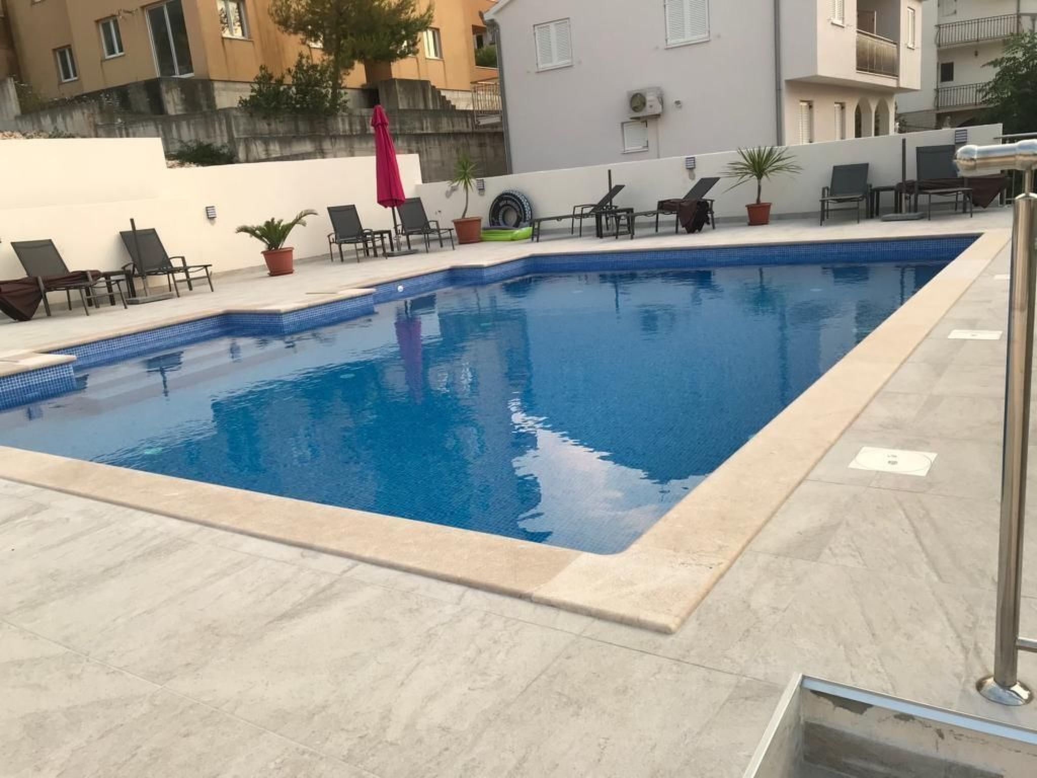 Una piscina rectangular con borde de azulejos, rodeada de sillones de descanso y plantas en macetas.