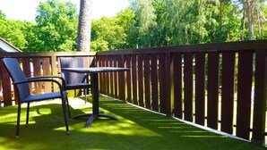 An outdoor patio with a table and two chairs, surrounded by a wooden deck and lush greenery.