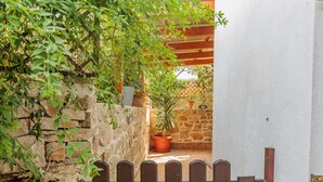 Un mur de pierre avec une porte en bois, des plantes en pot et une tonnelle en bois.