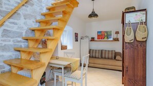 Un salon chaleureux avec un escalier en bois, un canapé blanc, une table à manger avec des chaises et un radiateur.