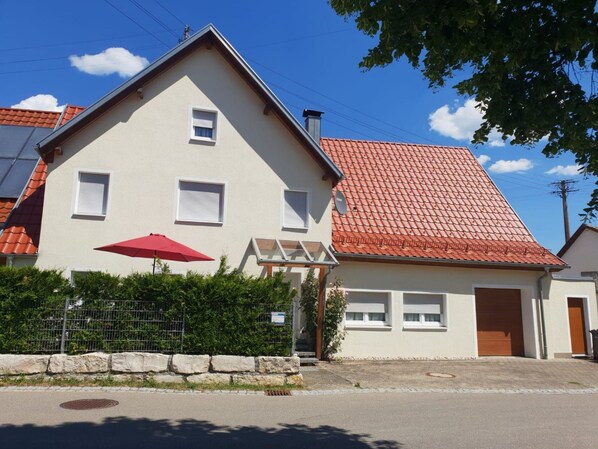 Un bâtiment à deux étages, avec un toit recouvert de tuiles rouges, un petit balcon et un parasol rouge.