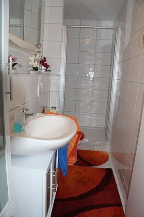 Une salle de bain avec un lavabo blanc, un miroir, une douche et un tapis rouge.