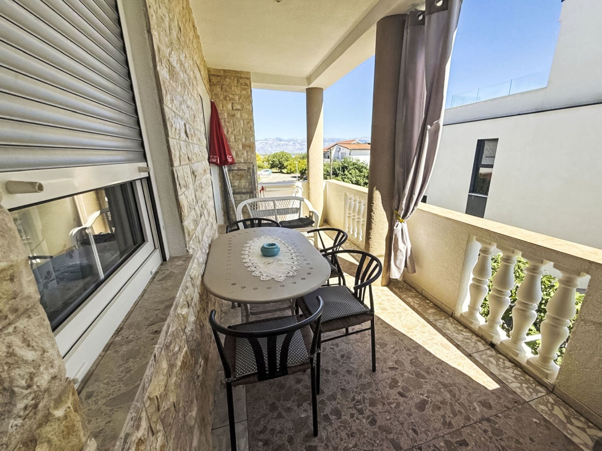 A balcony with a table and chairs, a red umbrella, and a view of the landscape.